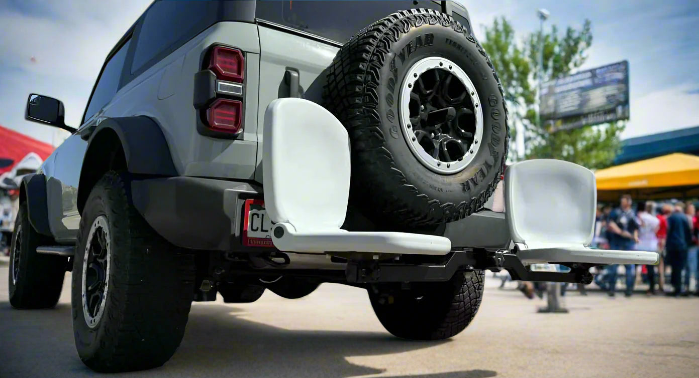 Gray off-road vehicle with a spare tire mounted on a trailer hitch in a parking lot.
