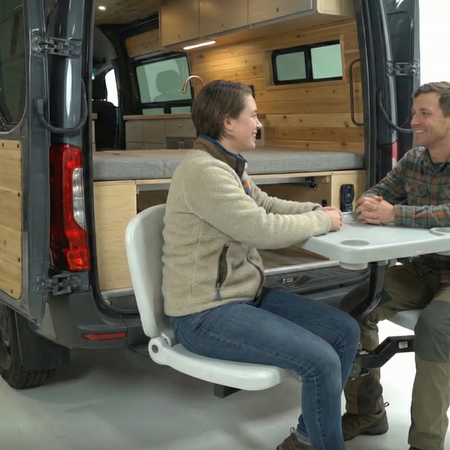Two people sitting on Van life accessory Tailbreaker at the rear of a van, set against a white background