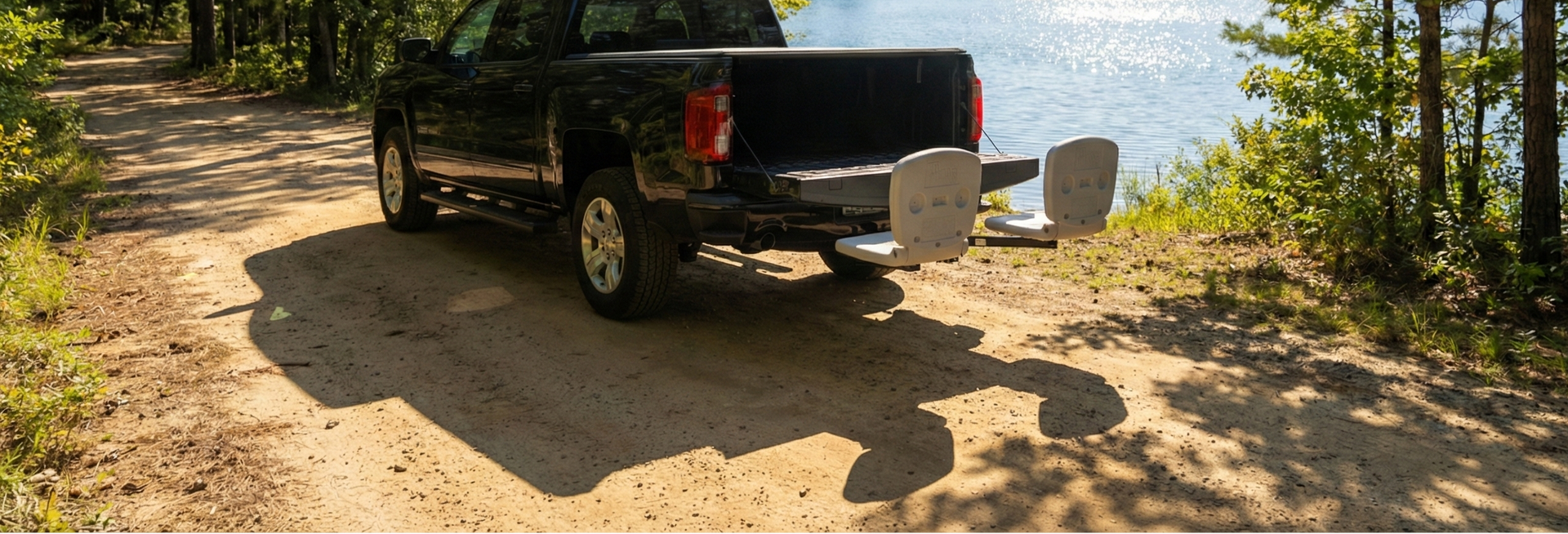 Black pickup truck with a tailbreaker  parked on a dirt road near a lake surrounded by trees.