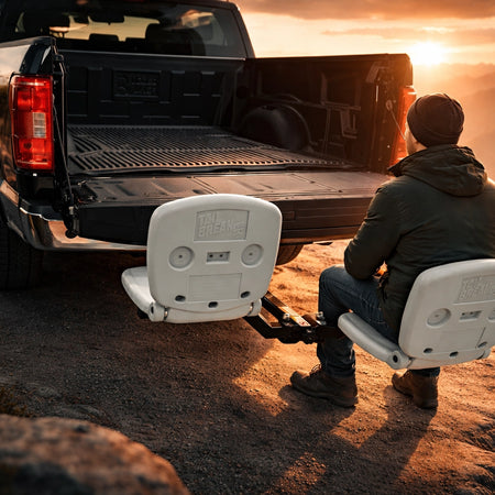 Person sitting on hitch seat tailbreaker in the back of a truck with a scenic mountain view at sunset.